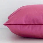 Lateral angle image of a velvet square cushion. The solid colour blush is highlighted along its seams.