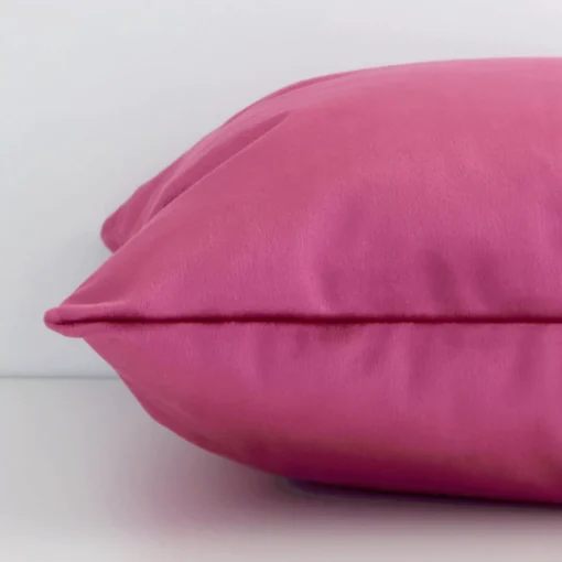 Lateral angle image of a velvet square cushion. The solid colour blush is highlighted along its seams.