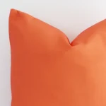 The corner of this coral outdoor cushion is shown close up. The finer detail of its square design can be seen.