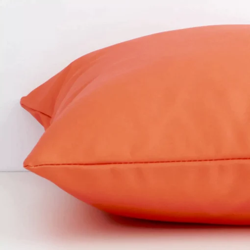 Coral solid-coloured cushion cover laid on its back side. The image shows a side-on view of the outdoor material and its square dimensions.