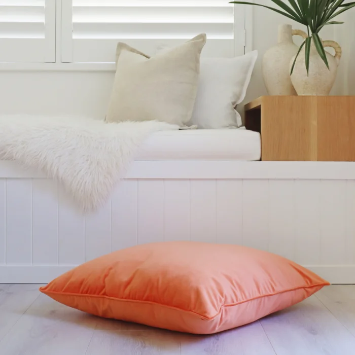 Coral coloured floor cushion styled in a white sitting room