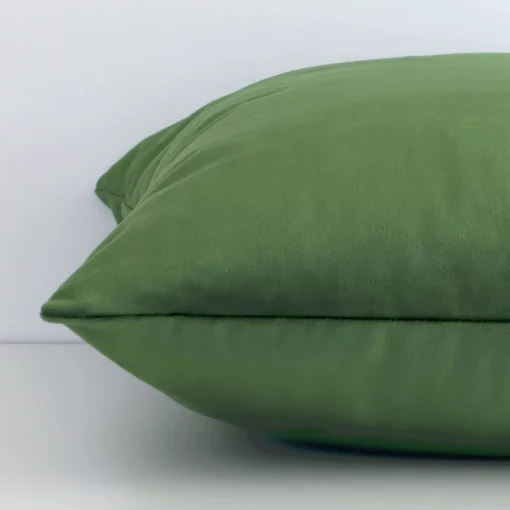 Solid colour forest green cushion laid horizontally. This perspective shows the edge of the velvet fabric and its square shape.