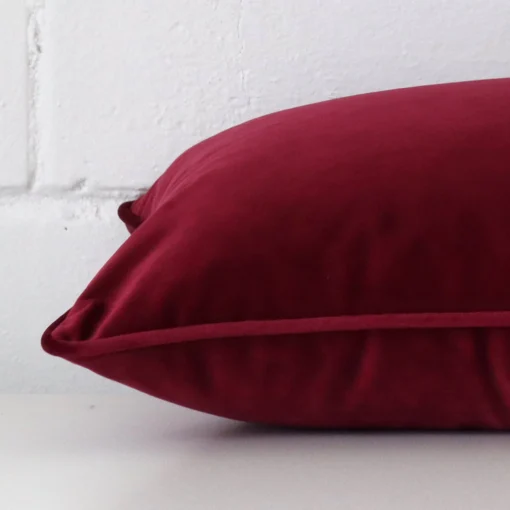 A maroon cushion arranged sideways in front of a wall. The rectangle size and velvet fabric are shown and the seams are clearly visible.