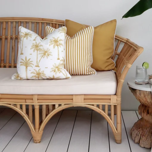 A rattan seat adorned with a set of 3 mustard outdoor couch cushions.