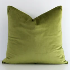 An attractive solid-coloured velvet cushion in front of a white brick wall. It has a rectangle shape and is olive in colour.