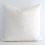 Lovely square white and beige cushion positioned in front of white wall. Its geometric style pops on the outdoor fabric.