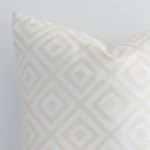 Close range image of white and beige geometric cushion. The square size and outdoor material can be seen in detail.