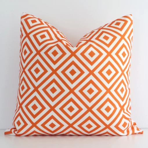 Orange geometric printed cushion cover sits against a white wall. It is constructed from a superior looking outdoor material and has square shape.