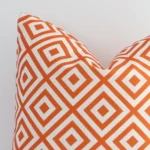 Close up view showing a corner of this geometric outdoor cushion in a square size and with orange print colouring.