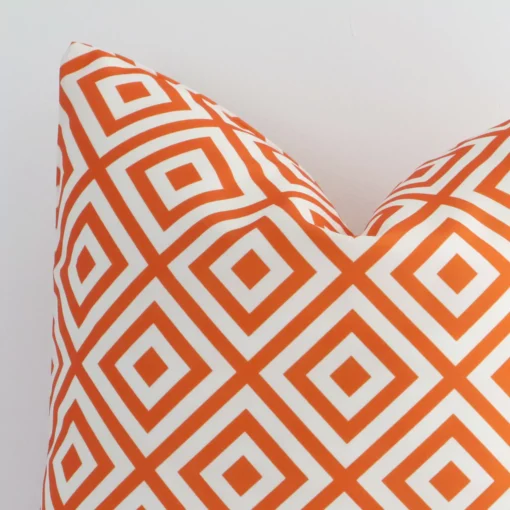 Close up view showing a corner of this geometric outdoor cushion in a square size and with orange print colouring.