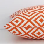 Squareoutdoor cushion cover positioned flat to show seams. The orange hue of its geometric design is shown between front and rear fabric panels.