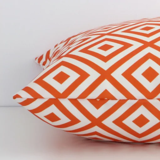 Squareoutdoor cushion cover positioned flat to show seams. The orange hue of its geometric design is shown between front and rear fabric panels.