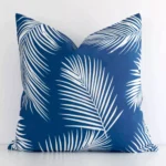 A white wall that has a palm designed blue cushion cover positioned in front of it. It has an exquisite outdoor material and a lovely square shape.