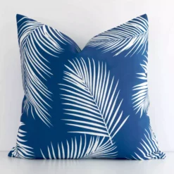 A white wall that has a palm designed blue cushion cover positioned in front of it. It has an exquisite outdoor material and a lovely square shape.