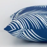 An outdoor blue cushion cover shown laying on its side. The palm design and its square size are shown side on.