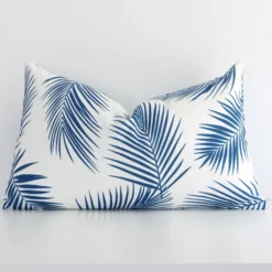 An outdoor rectangular cushion cover that has a unique palm design is shown vertically against a white wall. It has a wonderful blue print colour.