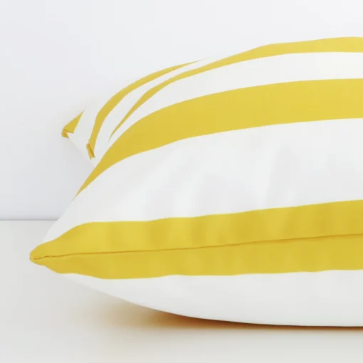 Close side shot of this yellow outdoor cushion cover. The viewpoint shows how the large design and stripe decorative finish meet along its edge.