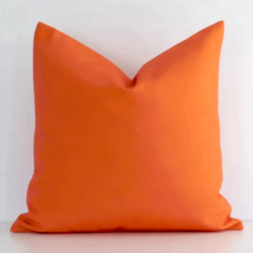 Square outdoor cushion cover in orange colour sitting upright in front of a white wall. It has been made from a quality outdoor material.