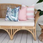 A set of 3 tropical pink outdoor couch cushions is displayed on a corner of a rattan seat.