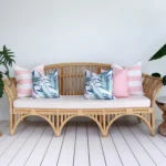 A rattan seat positioned between two leafy plants with a set of 5 pink outdoor cushions.
