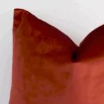 A velvet square cushion’s corner has been enlarged in this shot. The detail of the solid rust colour is visible.