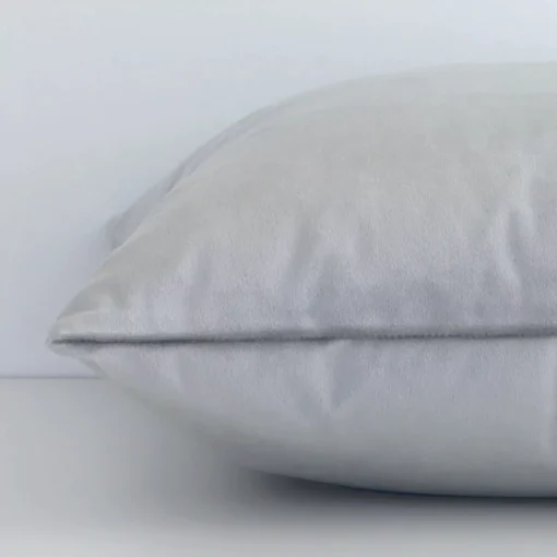 Horizontal edge of solid-coloured square cushion cover is shown. The velvet fabric and silver tone can be seen from this side view.