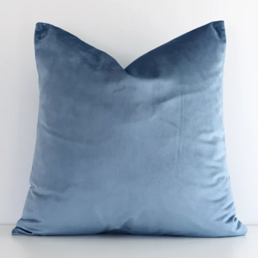 Stone blue solid-coloured cushion positioned in front of a white wall. It has square shape and is made from a velvet material.