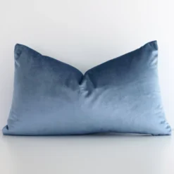 A lovely rectangular stone blue cushion cover arranged in front of a white wall. The solid colour style complements the velvet material.