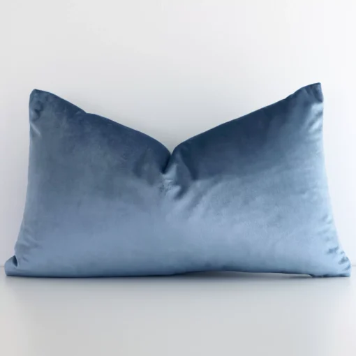 A lovely rectangular stone blue cushion cover arranged in front of a white wall. The solid colour style complements the velvet material.