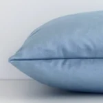 Lateral angle image of a velvet rectangular cushion. The stone blue colour and solid colour design are highlighted along its seams.