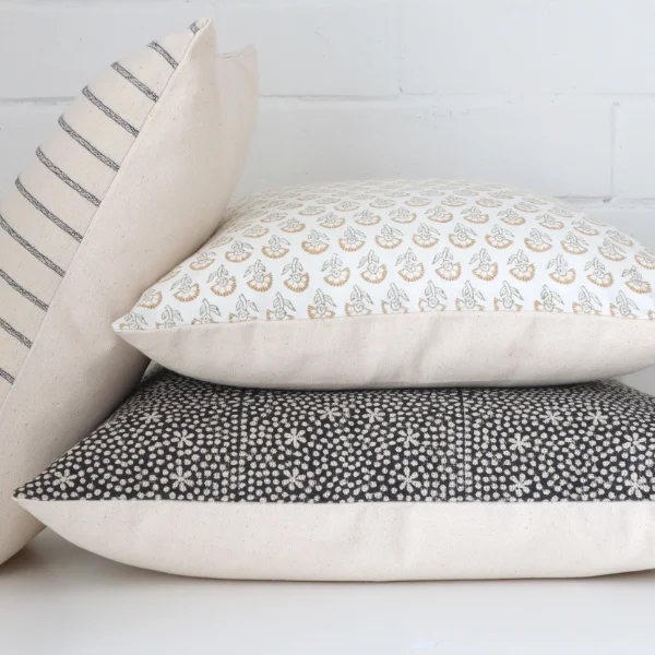 A white wall with block printed cushions arranged in front of it.